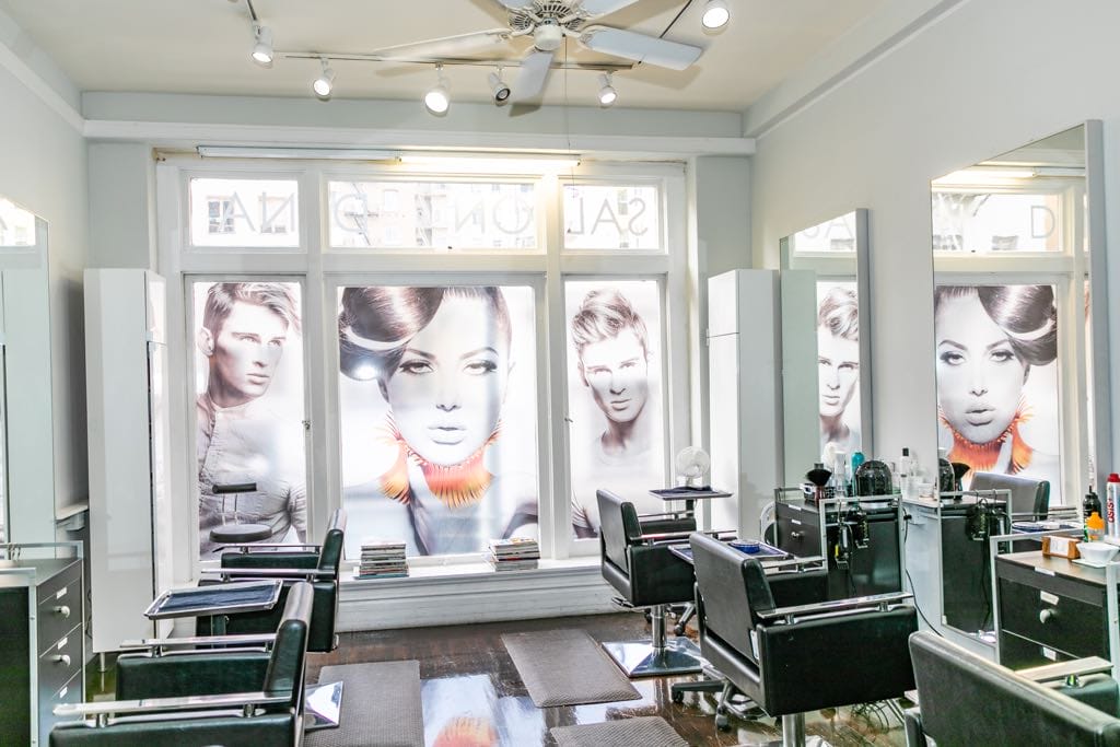 Interior of a hair salon with black styling chairs and large posters of models in the windows.